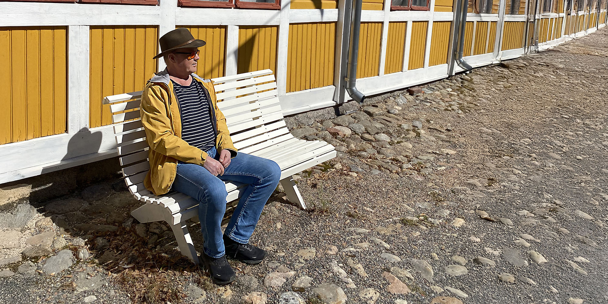 Pekka istuu valkoisella puistonpenkillä katsoen etuoikealle.